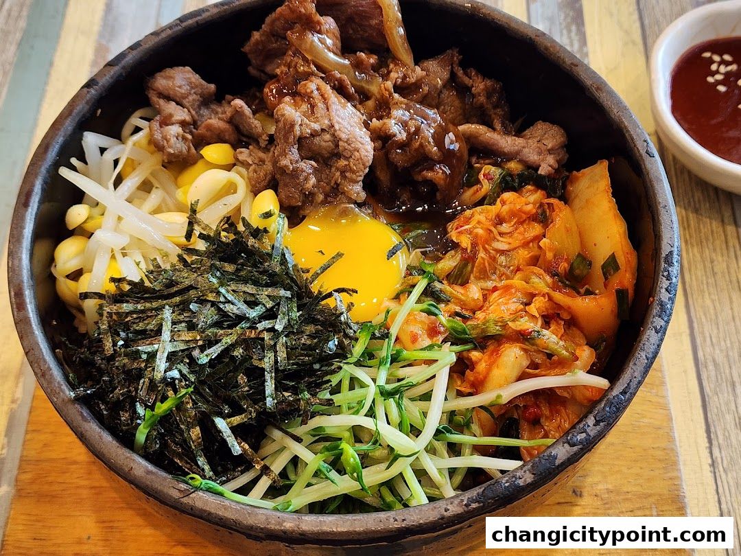 A close-up of a delicious bibimbap served in a stone bowl with a side of sauce.