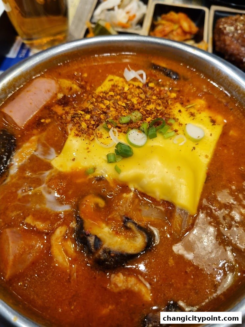 A close-up of a steaming hot pot dish with cheese, chili flakes, and various ingredients.