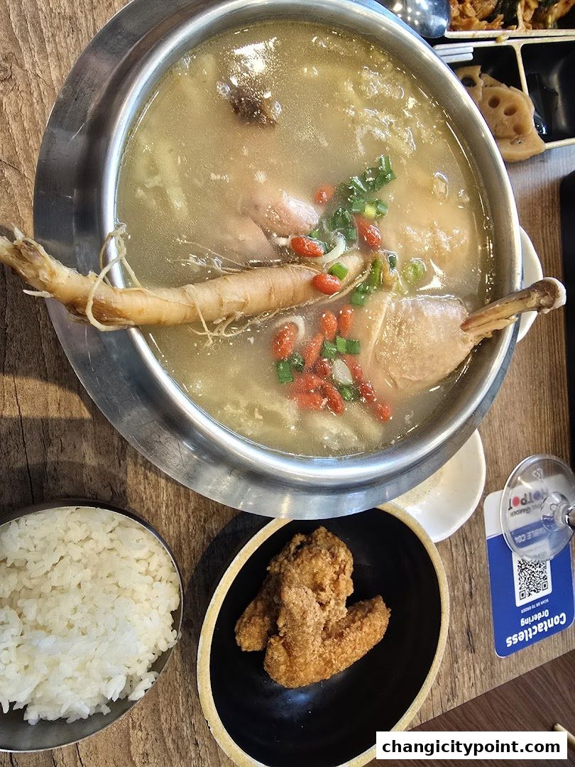 A steaming pot of ginseng chicken soup with rice and fried chicken wings.
