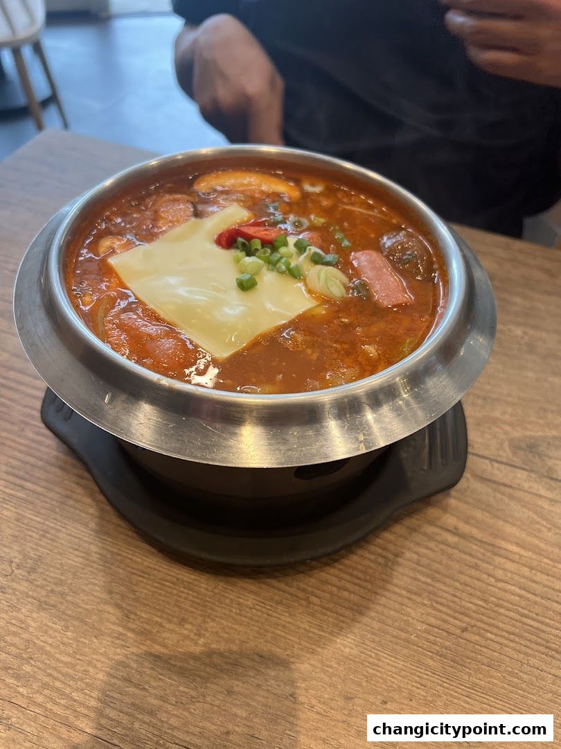 A steaming bowl of Korean stew with cheese, sausage, and vegetables.