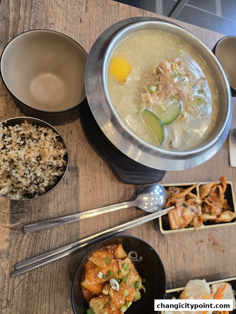 A steaming hot pot dish with rice, kimchi, and other Korean side dishes.