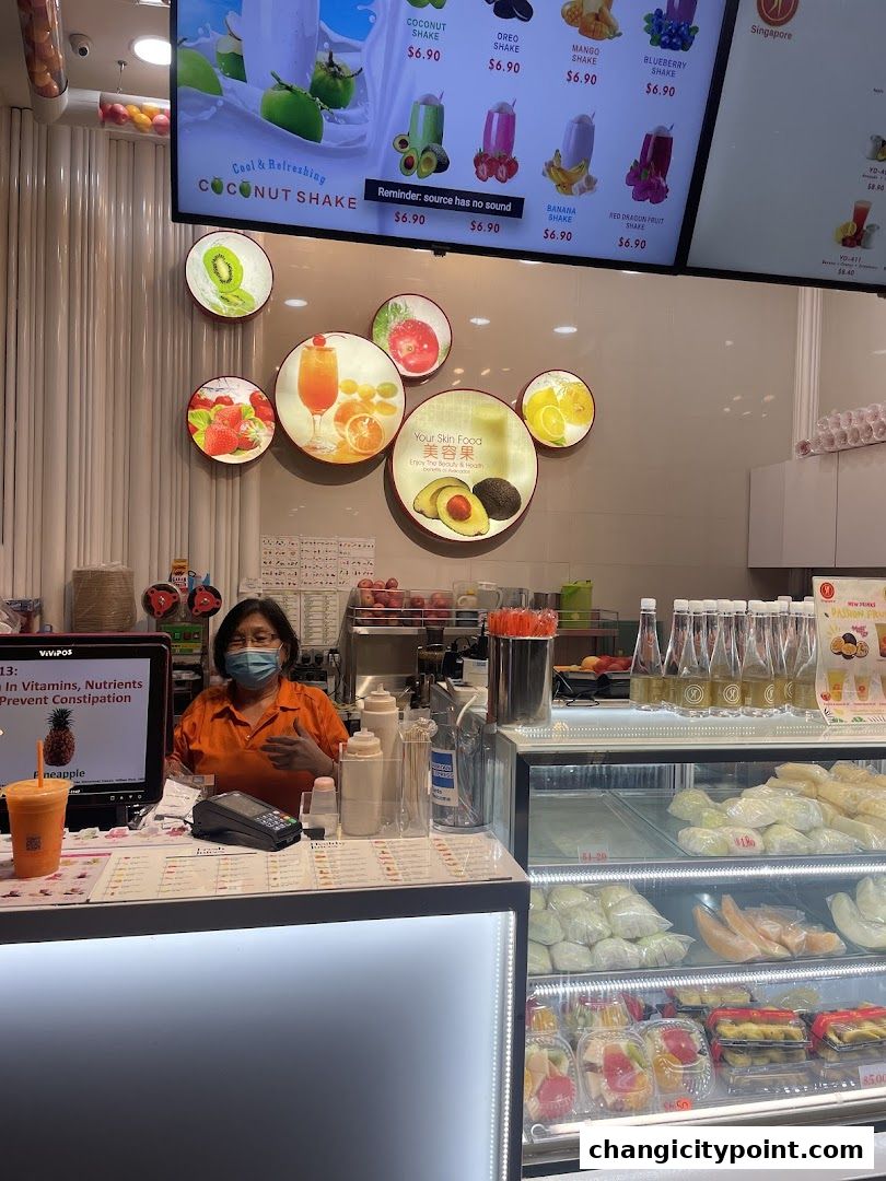 A juice bar counter with a staff member, menu board, and display of fresh fruits and juices.