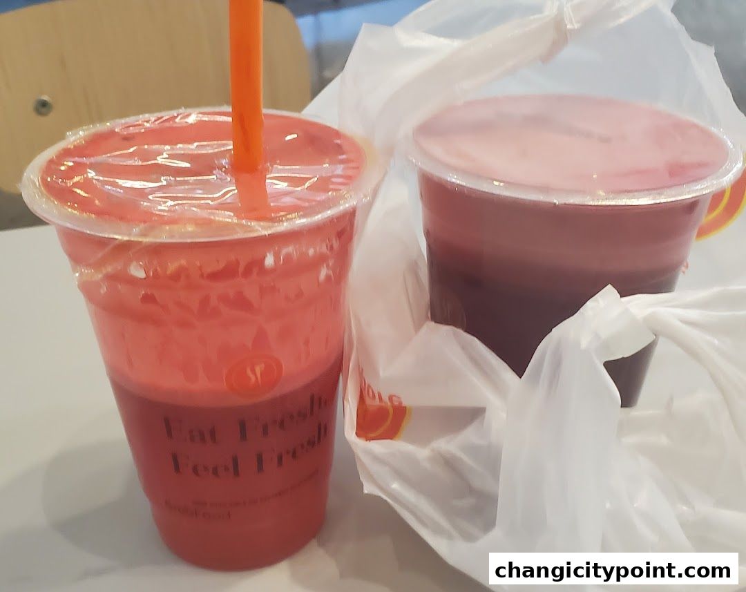 Two takeaway cups of colorful fruit juices, one red and one dark red, in plastic bags.