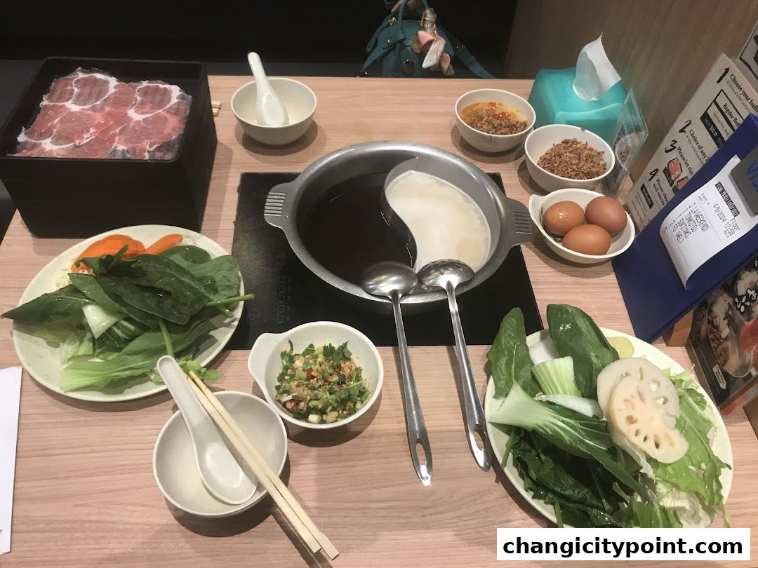 A table set for shabu-shabu with thinly sliced meat, vegetables, broth, and condiments.