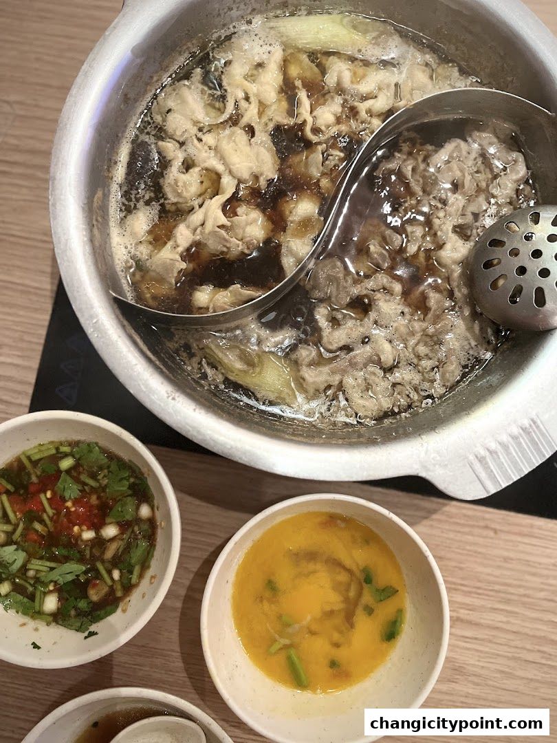 A split hot pot with meat and vegetables, served with dipping sauces.