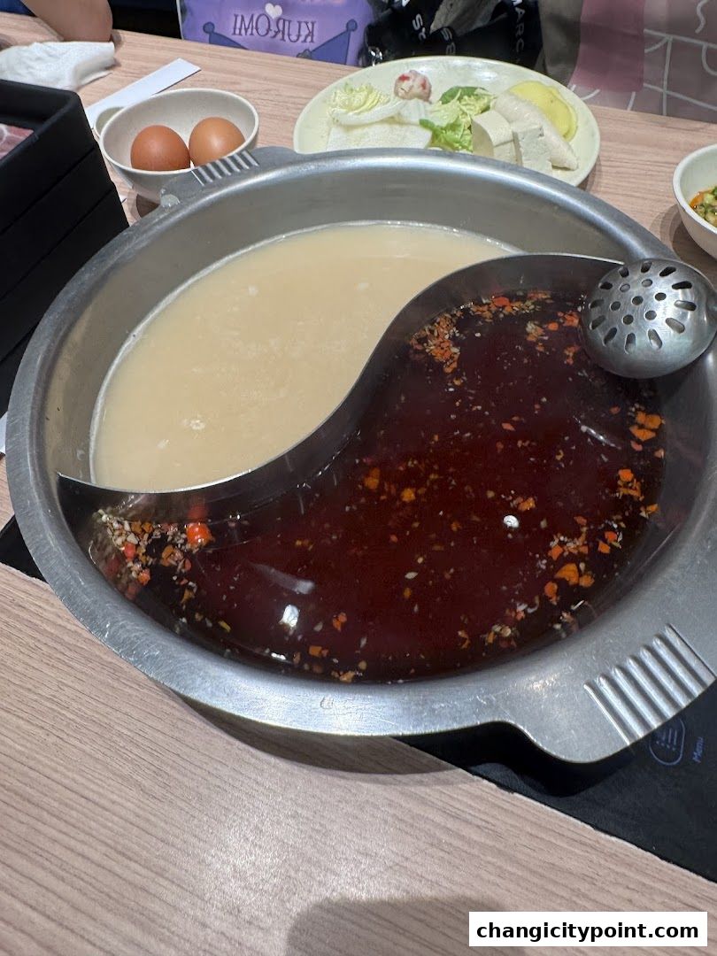 A yin-yang shaped hot pot with two broths, served with eggs and vegetables.