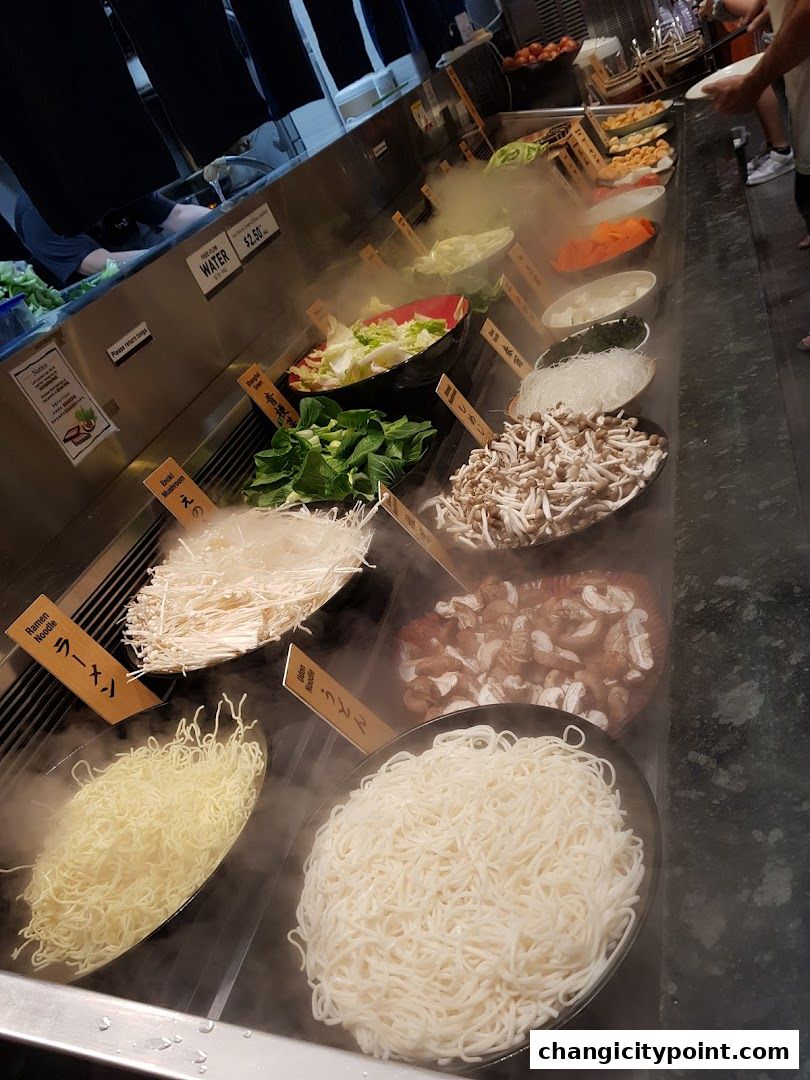 A buffet-style display of fresh ingredients for hot pot, including various noodles, vegetables, and mushrooms.