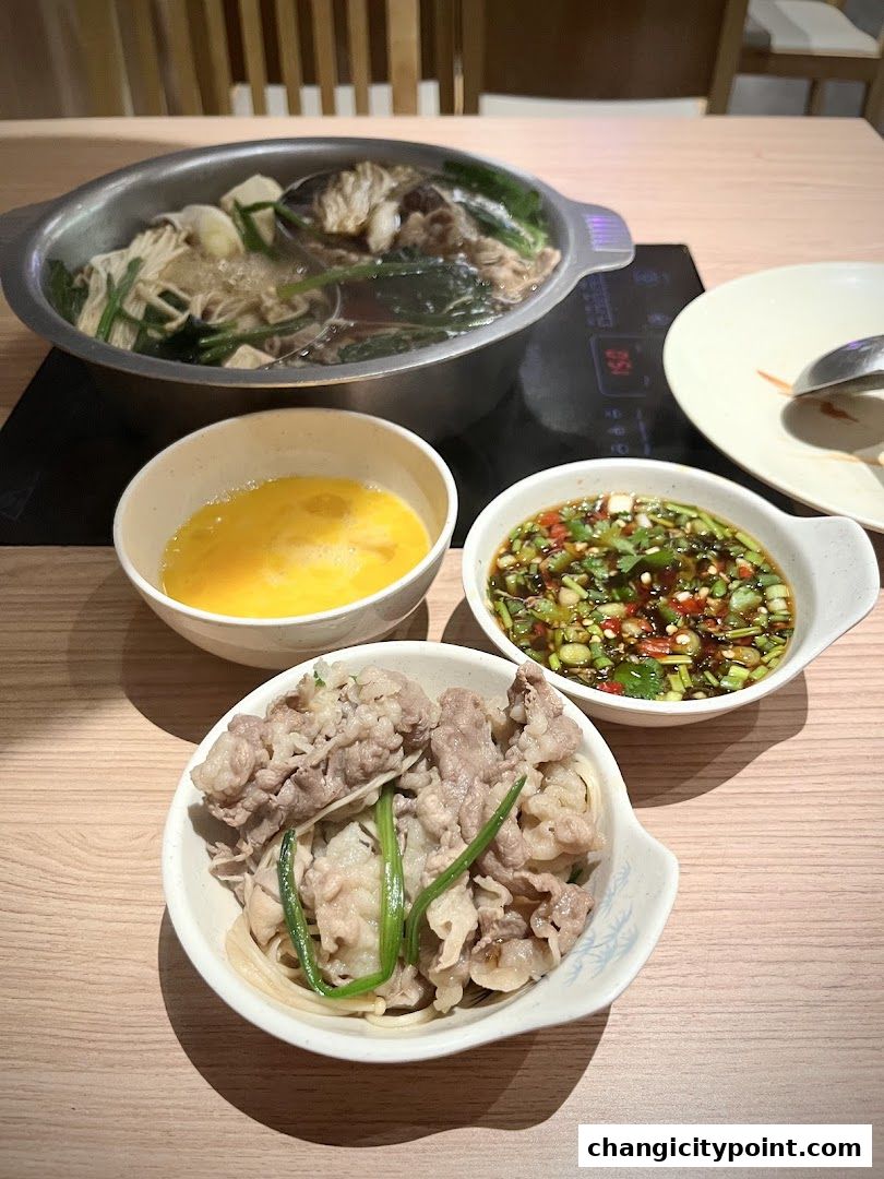 A steaming pot of shabu-shabu with thinly sliced beef, egg, and dipping sauce.
