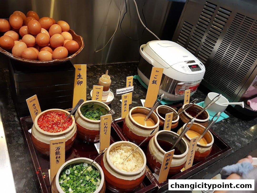 A variety of condiments and ingredients for shabu-shabu, including eggs, chili, and sauces.