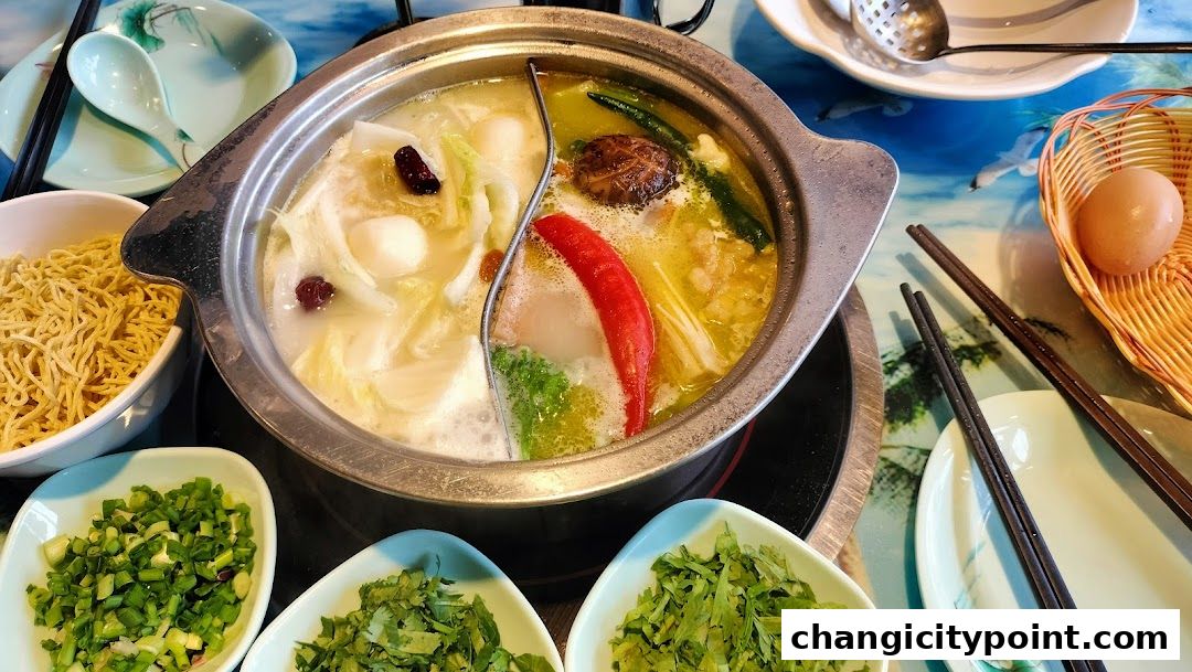A split hot pot with various ingredients and side dishes, including noodles and chopped herbs.