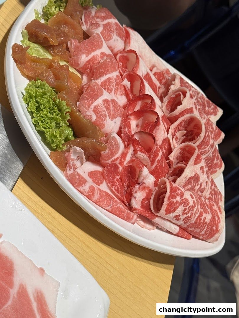 A platter of thinly sliced raw meats and some vegetables, ready for hot pot.