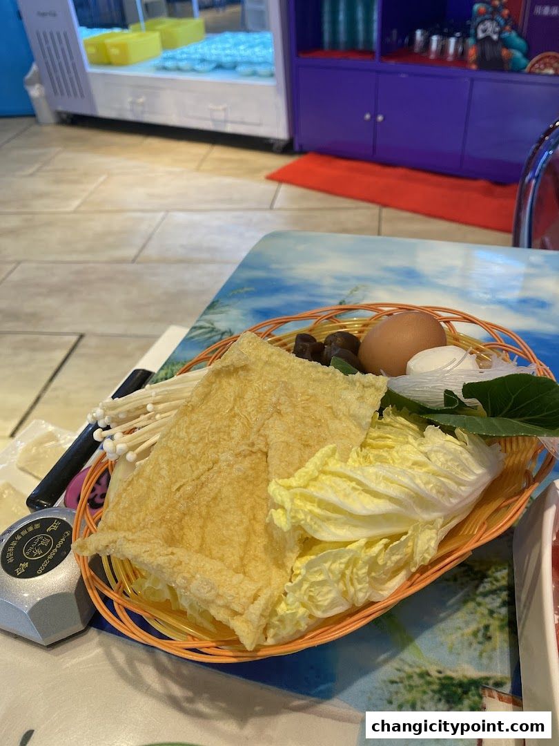 A basket of fresh hot pot ingredients including tofu skin, napa cabbage, enoki mushrooms, and an egg.