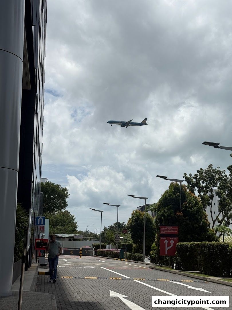 An airplane flies in the sky above a street with a man walking.