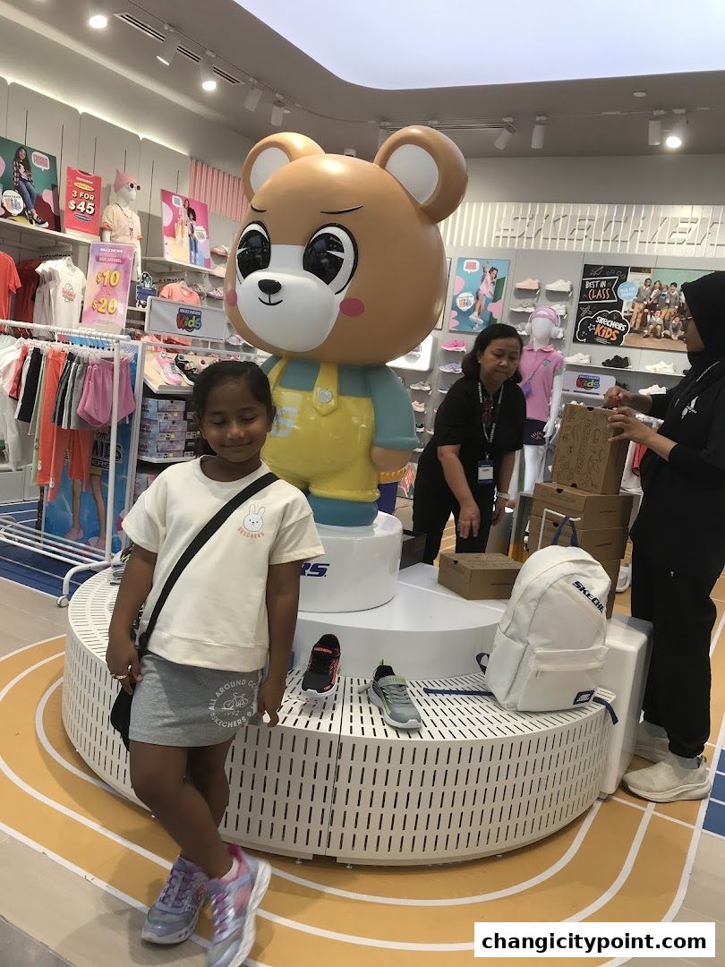 A young girl poses in front of a large bear mascot inside a Skechers store.
