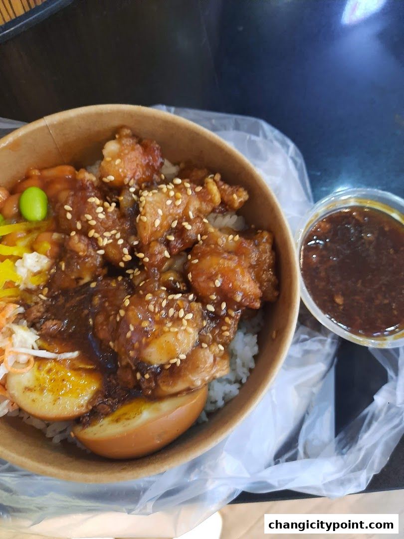 A close-up of a delicious bowl of rice topped with fried chicken and a side of sauce.