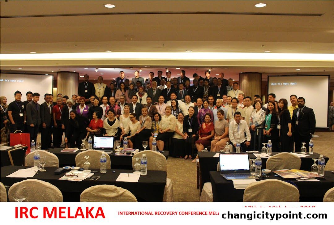 A large group of people pose for a photo at a conference in a hotel ballroom.