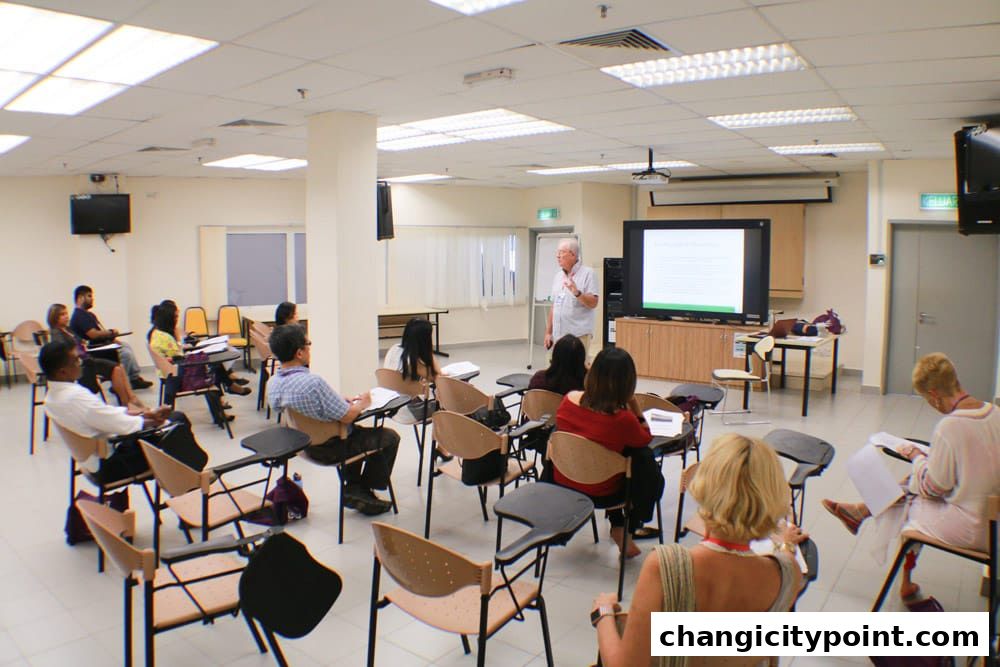 A lecture hall with a presenter and seated students taking notes.