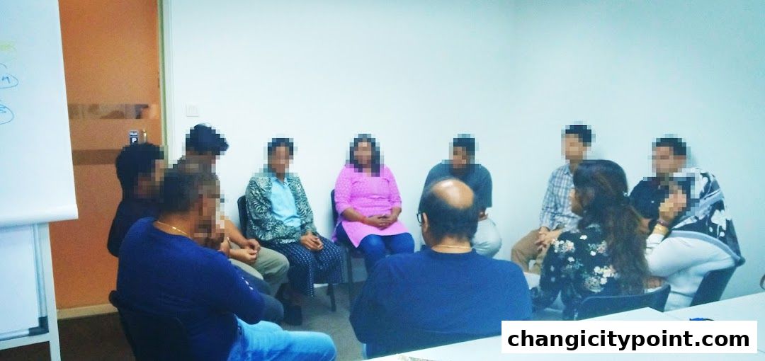 A group of people are seated in a circle in a room, possibly for a meeting or therapy session.