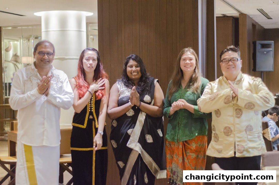 A group of five people in traditional attire, posing for a photo with hands clasped.