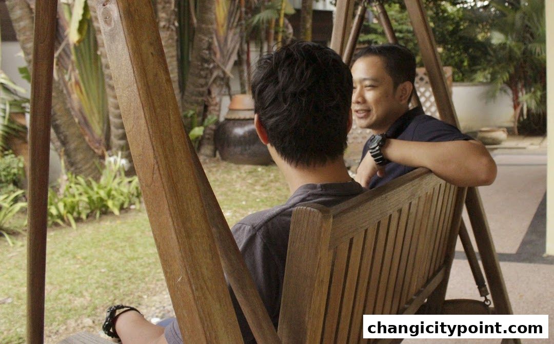 Two men relax on a wooden swing bench in a lush, tropical outdoor setting.