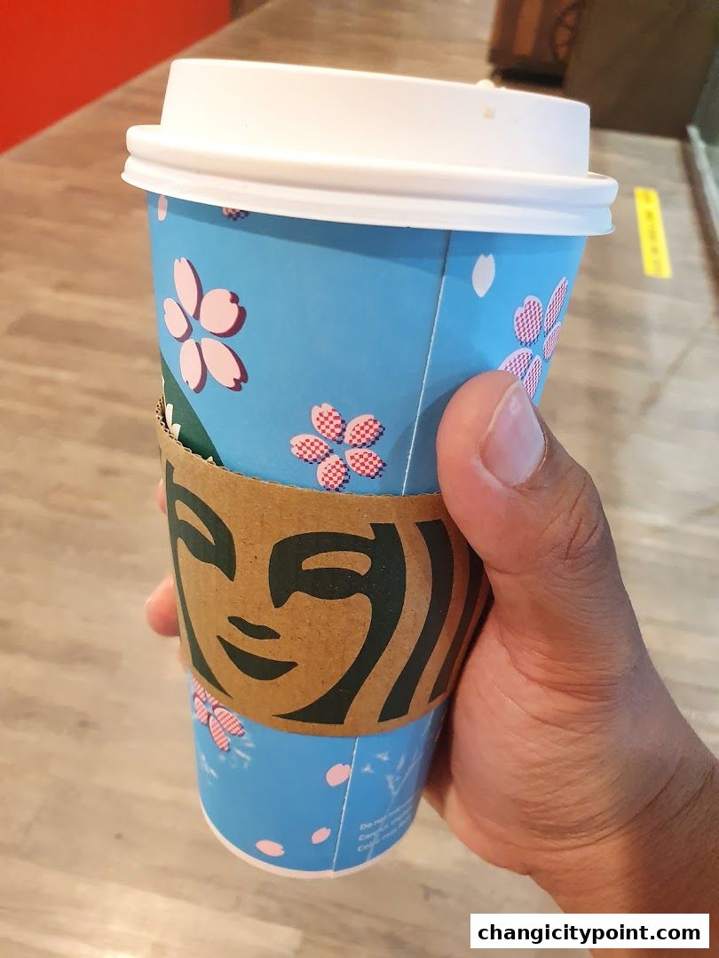 A hand holds a Starbucks cup with a cherry blossom design.