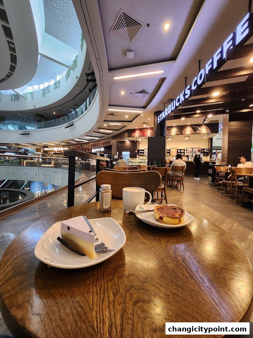 A table at Starbucks with coffee, cake, and a tart, overlooking a mall atrium.