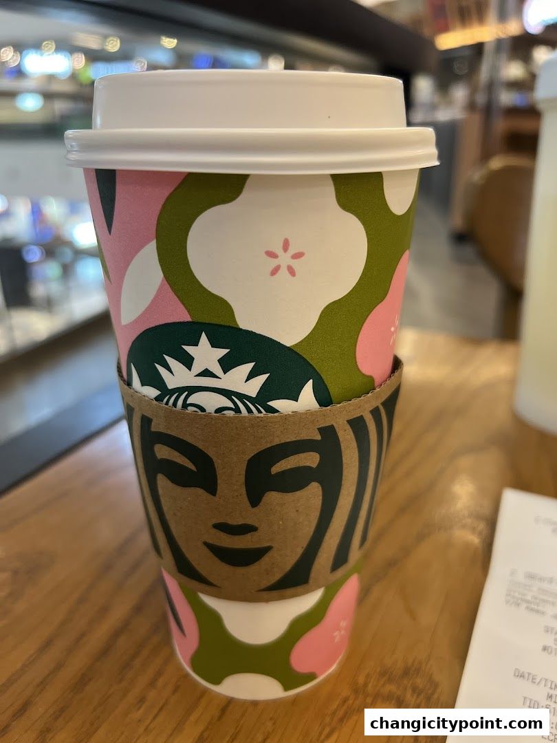 A Starbucks cup with a floral design and a coffee sleeve sits on a wooden table.