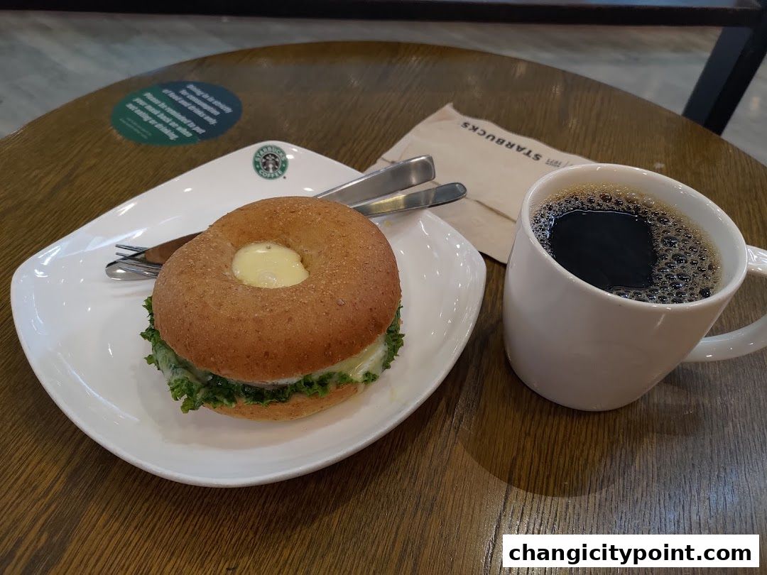A Starbucks bagel sandwich and a cup of black coffee on a wooden table.