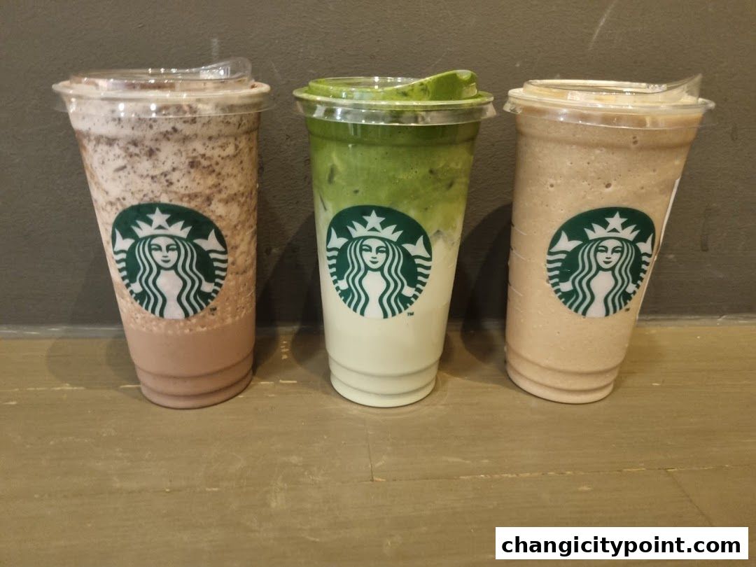 Three Starbucks beverages lined up against a grey wall on a wooden surface.