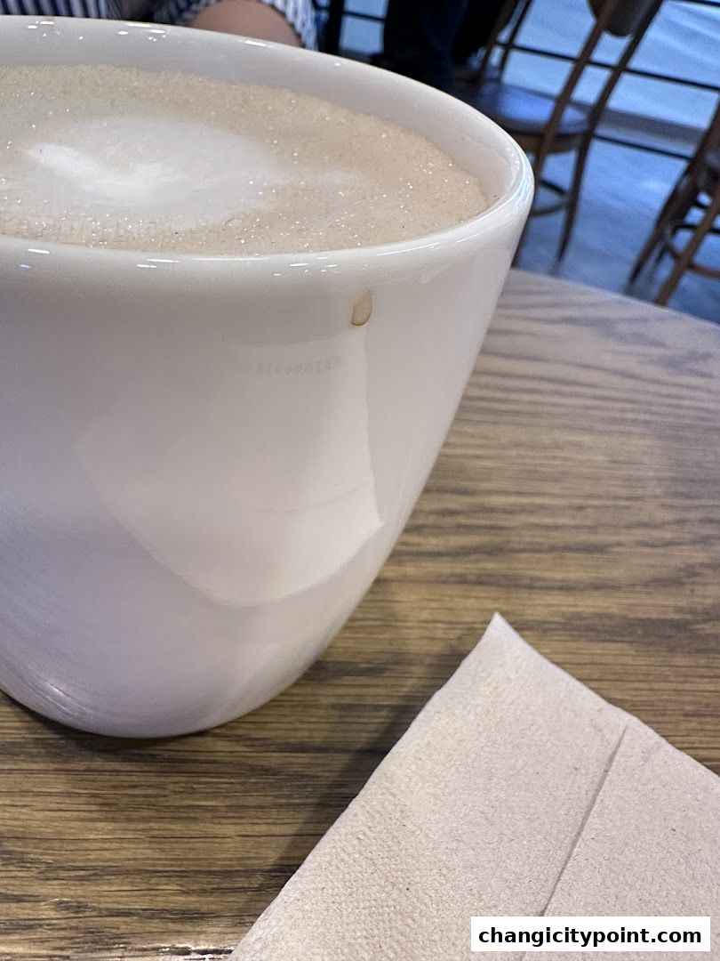 A close-up of a white mug filled with frothy coffee on a wooden table.