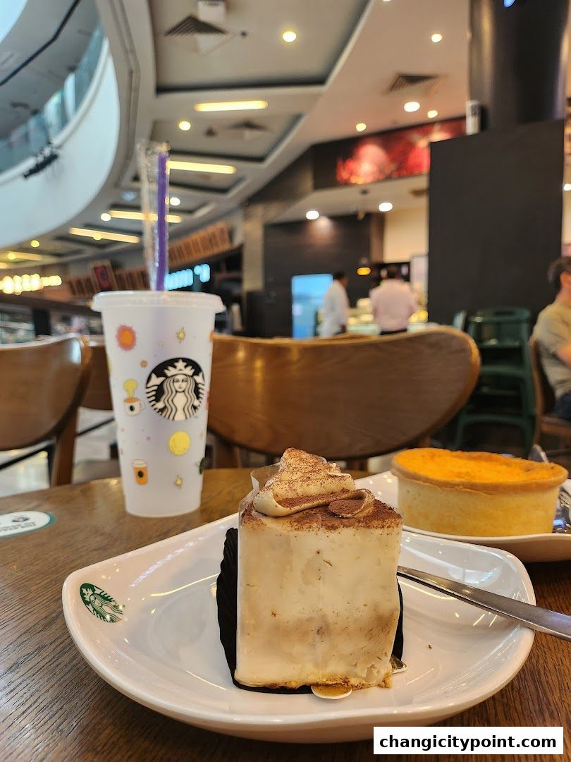 A slice of cake and a drink from Starbucks on a table.