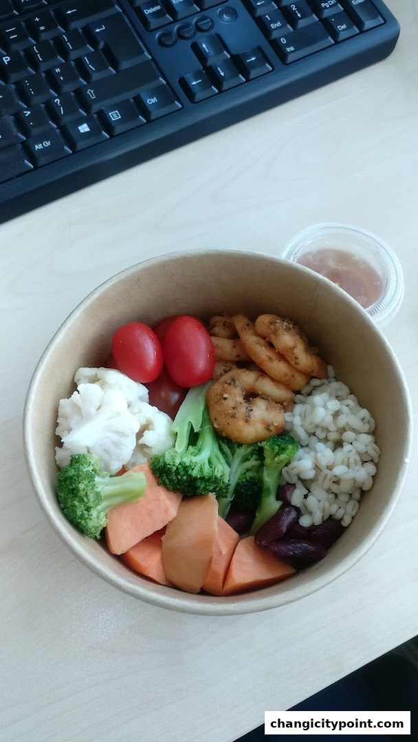 A healthy bowl of food with shrimp, vegetables, and grains, next to a keyboard.