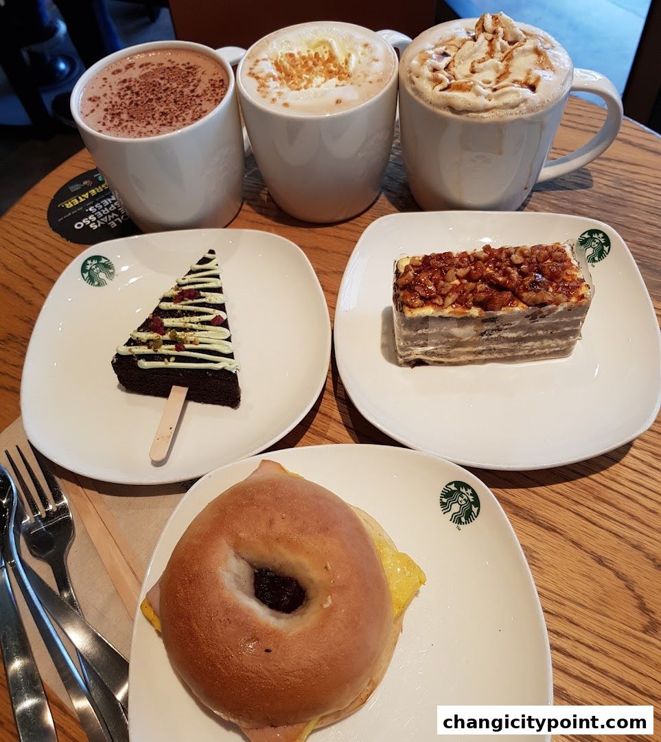 A spread of Starbucks beverages, pastries, and a bagel sandwich on a wooden table.