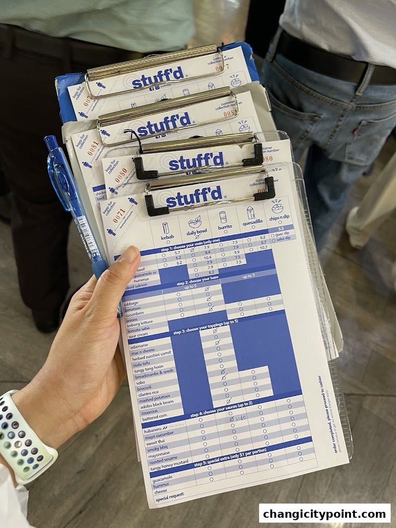 A hand holds several 'Stuffd' order forms with a pen, detailing food choices.