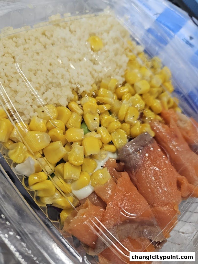 A clear plastic container filled with couscous, corn, and sliced salmon.