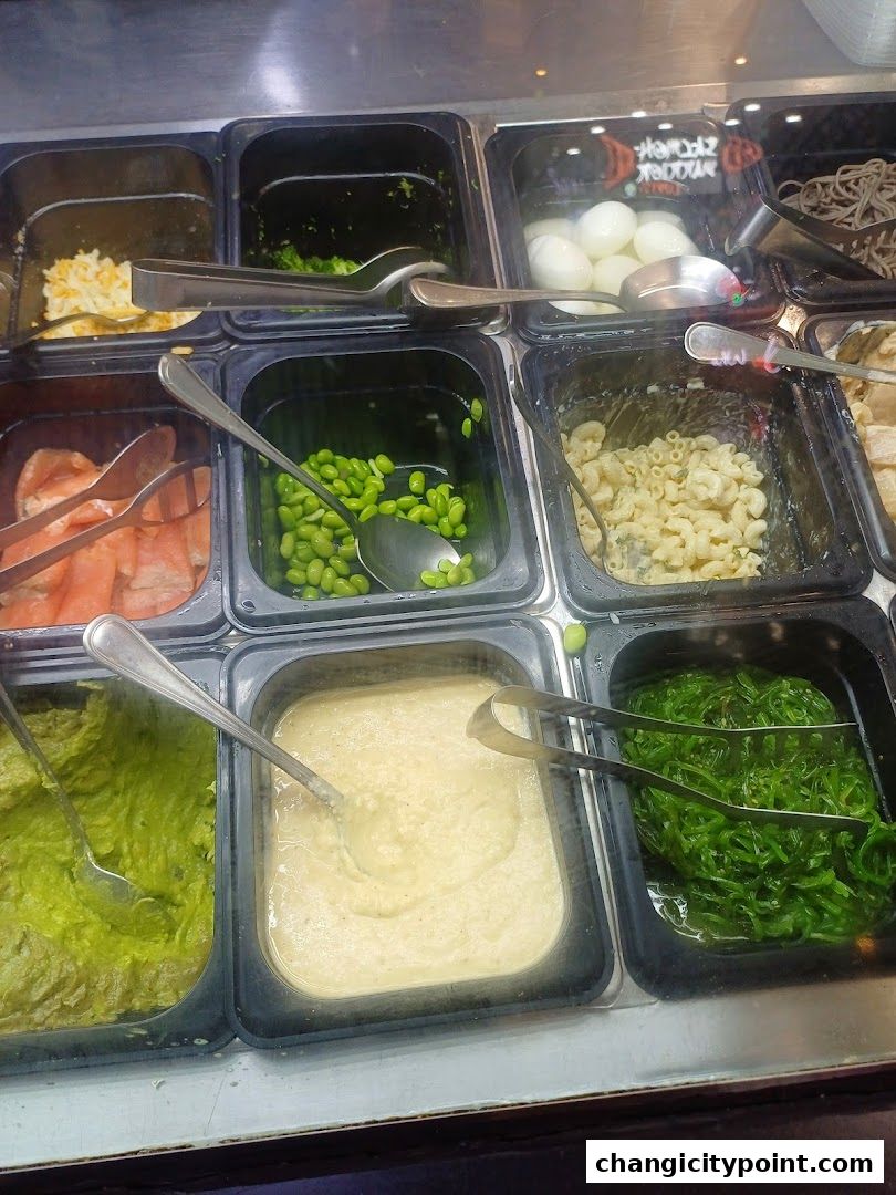 A display of various food ingredients in containers, including salmon, edamame, pasta, and mashed avocado.