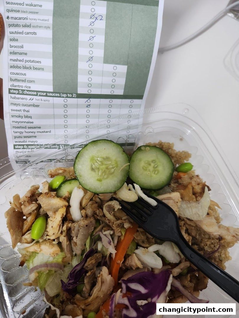 A close-up of a customizable bowl with chicken, vegetables, and quinoa, next to a menu.