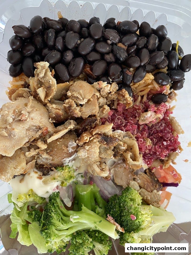A clear plastic container filled with a colorful and healthy meal, featuring black beans, chicken, quinoa, and broccoli.