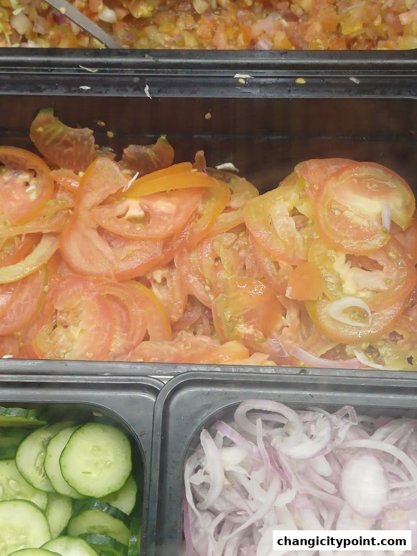 Freshly sliced tomatoes, cucumbers, and onions displayed in a food service counter.