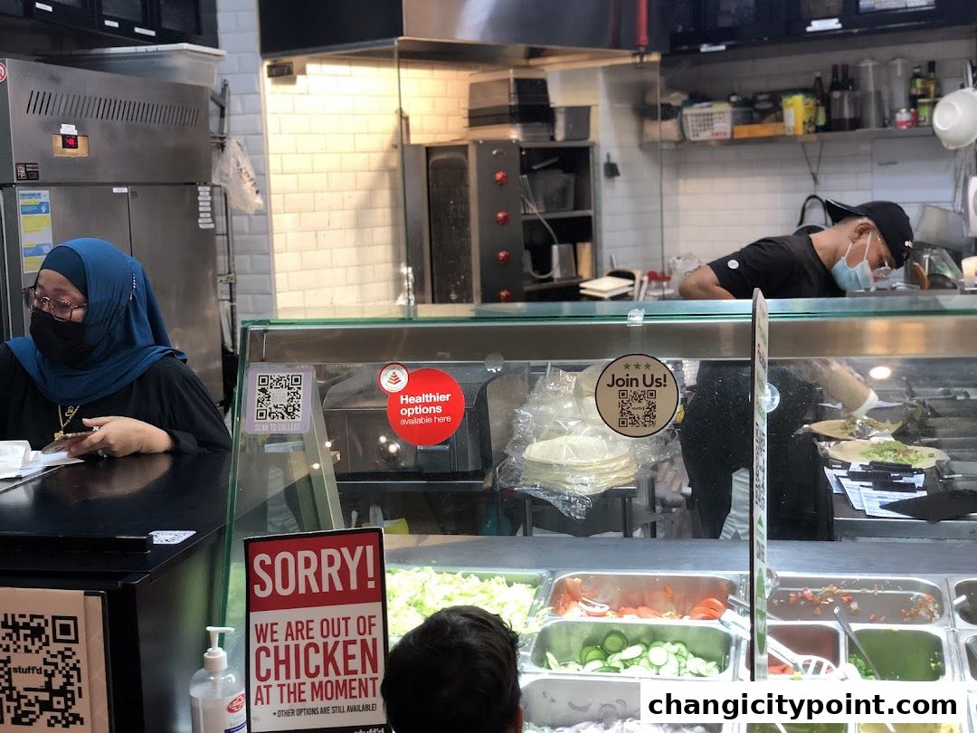 A food service counter with staff preparing orders and fresh ingredients displayed.