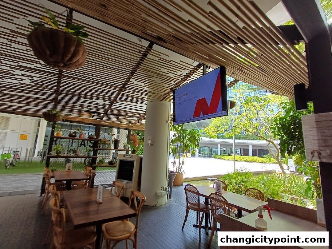 An outdoor seating area with tables and chairs, plants, and a digital screen.