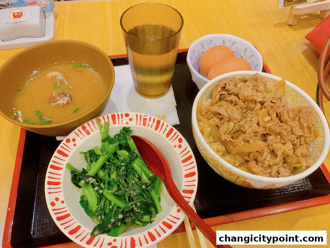 A delicious Sukiya Gyudon meal with miso soup, greens, and a drink.