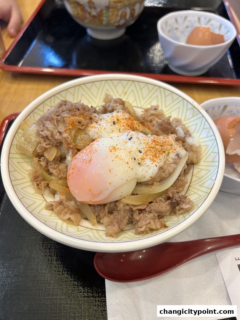A close-up of a delicious Sukiya Gyudon bowl with a soft-boiled egg and seasoned beef.