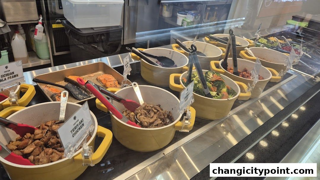 A display of various cooked food items in yellow bowls with tongs, including salmon and chicken.