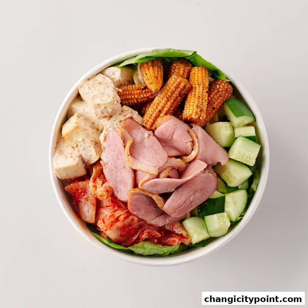 A bowl of salad with duck, tofu, corn, kimchi, and cucumber.