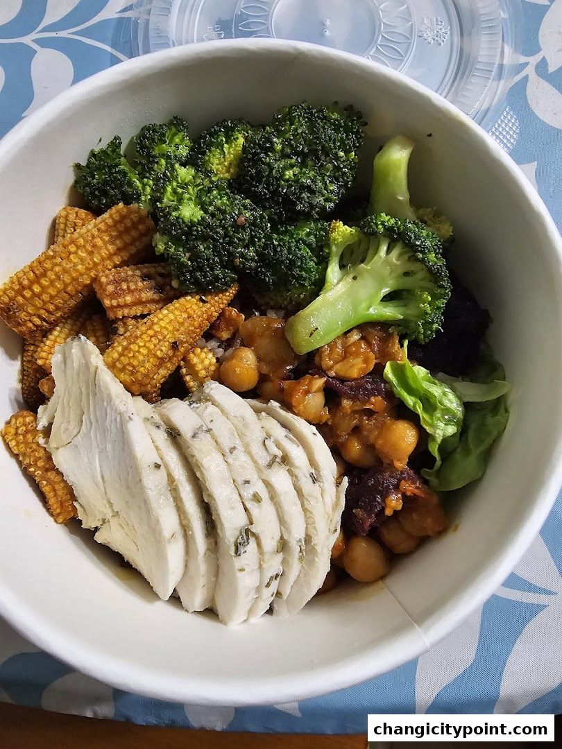 A healthy bowl of food with sliced chicken, broccoli, corn, and chickpeas.