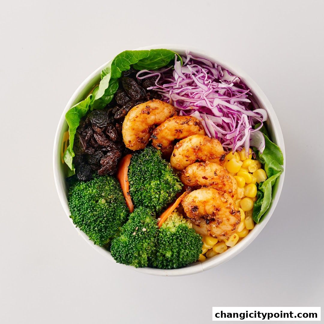 A vibrant bowl of salad with shrimp, broccoli, corn, raisins, and red cabbage.