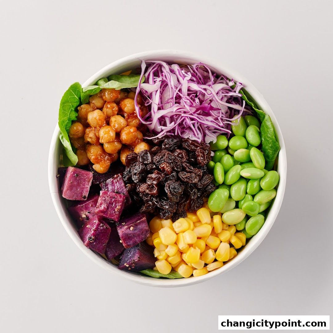 A vibrant bowl filled with healthy ingredients like chickpeas, purple sweet potato, edamame, corn, raisins, and red cabbage.