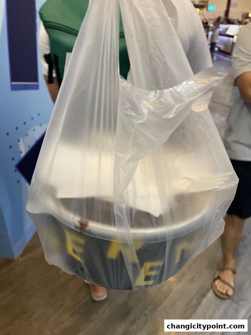 A person holds a plastic bag containing a black bowl with yellow lettering.