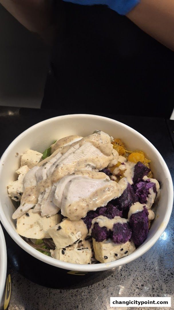 A bowl of healthy food with sliced chicken, tofu, purple sweet potato, and dressing.